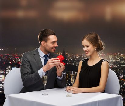 restaurant, couple and holiday concept - excited young woman looking at boyfriend with gift box at restaurant