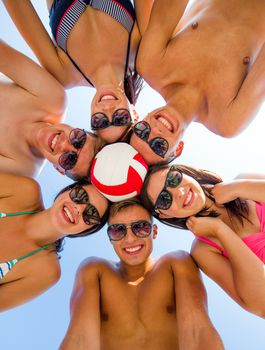 friendship, happiness, summer vacation, holidays and people concept - group of smiling friends wearing swimwear standing in circle with volleyball over blue sky