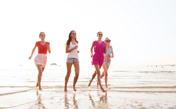 summer vacation, holidays, travel and people concept - group of smiling young women in sunglasses and casual clothes running on beach