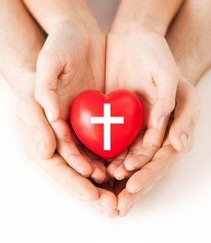 religion, christianity and charity concept - family couple hands holding red heart with christian cross symbol