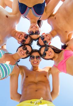 friendship, happiness, summer vacation, holidays and people concept - group of smiling friends wearing swimwear standing in circle over blue sky