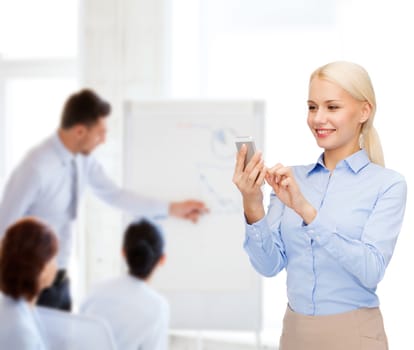 business, technology, education and people concept - smiling young businesswoman with smartphone in office