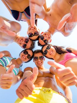 friendship, summer vacation, holidays, gesture and people concept - group of smiling friends wearing swimwear standing in circle and showing thumbs up over blue sky