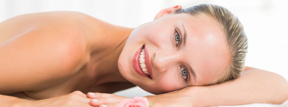 Peaceful blonde lying on towel smiling at camera at the health spa