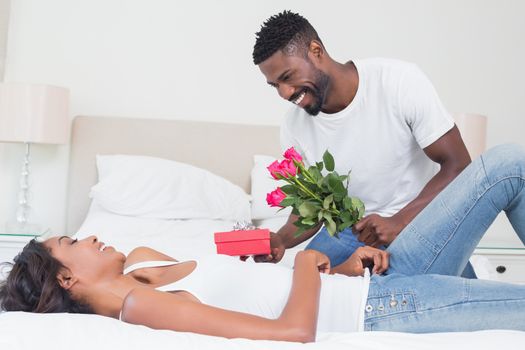 Romantic man giving roses to partner at home in bedroom