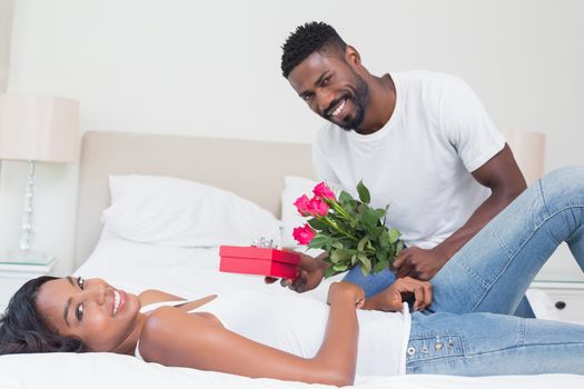 Romantic man giving roses to partner at home in bedroom