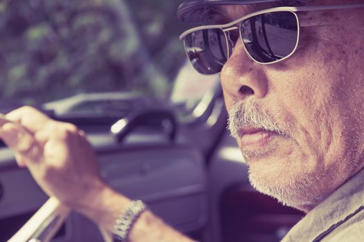 Close up image of older man with glasses driving a car