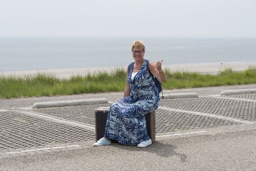 woman sitting on old suitcase and travel alomng the beach by hitchhiking