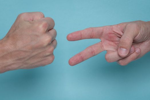 Men's hands playing rock, paper, scissors on a light blue background. One is throwing rock, the other is throwing scissors.