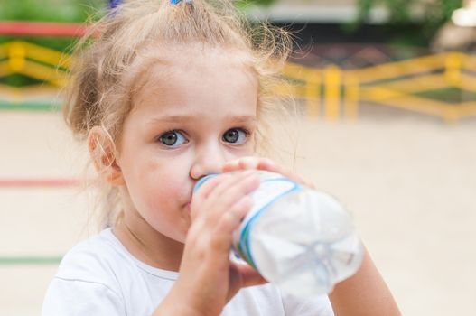 Three year old girl drinks from a bottle at the playground
