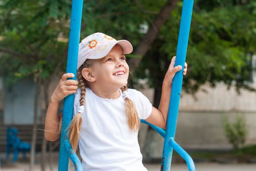 Happy five year old girl riding on a swing at the playground