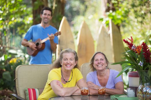 Pair of happy female friends near ukulele player outdoors