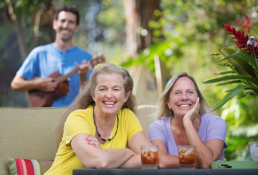 Pair of laughing female friends near ukulele player outdoors