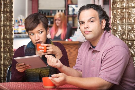 Pretty Hispanic woman reading tablet and ignoring boyfriend