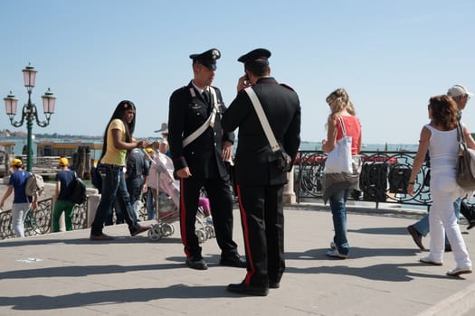 Two Carabinieri, from one of Italy's two police forces keepin a watch on activities as tourists pass by near Venice waterfront.
