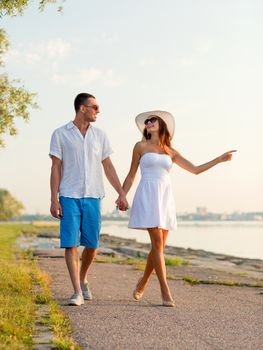 love, travel, tourism, gesture and people concept - smiling couple on summer vacation wearing sunglasses and pointing finger walking at seaside