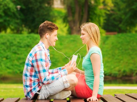 summer, vacation, holidays, technology and friendship concept - smiling couple with smartphone and earphones sitting on bench in park