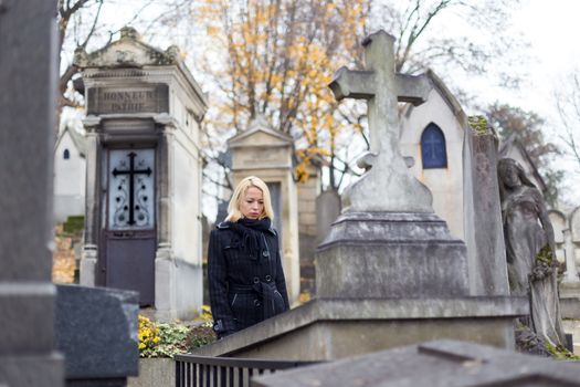 Solitary woman mourning by gravestone, remembering dead relatives in on Pere Lachaise cemetery in Paris, France.