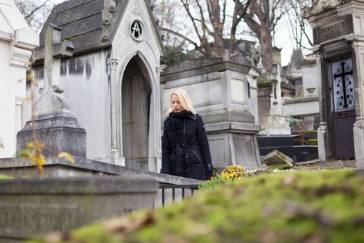 Solitary woman mourning by gravestone, remembering dead relatives in on Pere Lachaise cemetery in Paris, France.