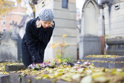 Solitary woman mourning by gravestone, remembering dead relatives in on Pere Lachaise cemetery in Paris, France.