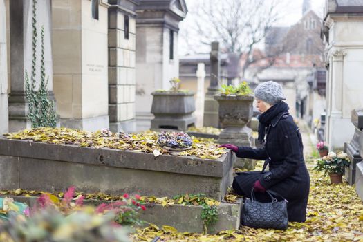 Solitary woman mourning with her hand on gravestone, remembering dead relatives in on Pere Lachaise cemetery in Paris, France.