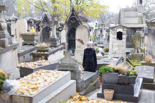 Solitary woman mourning by gravestone, remembering dead relatives in on Pere Lachaise cemetery in Paris, France.