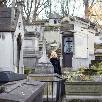 Solitary woman mourning by gravestone, remembering dead relatives in on Pere Lachaise cemetery in Paris, France.