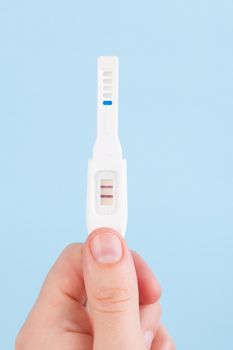 Male hand holding positive pregnancy test isolated on light blue background. Happy father.