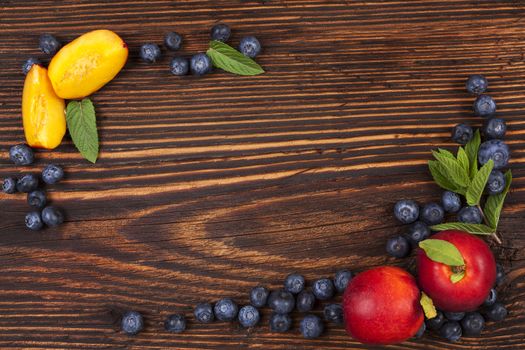 Fresh fruit background with copyspace. Blueberries and nectarines and mint leaves on wooden background, top view.