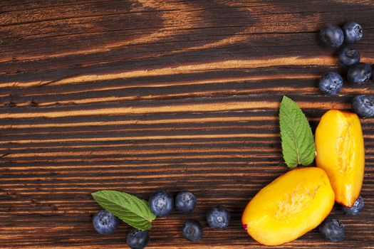 Fresh fruit background with copyspace. Blueberries and nectarines and mint leaves on wooden background, top view.