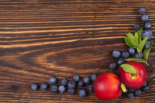 Fresh fruit background with copyspace. Blueberries and nectarines and mint leaves on wooden background, top view.