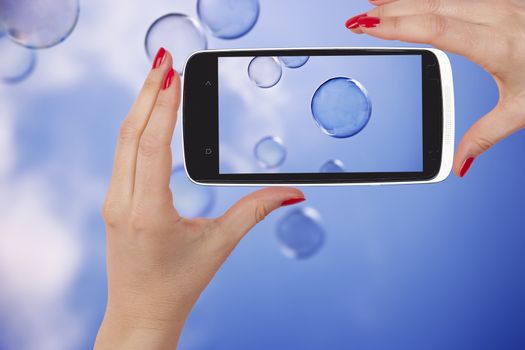 Woman taking a snapshot of flying soap bubbles in the air. Sharing. 