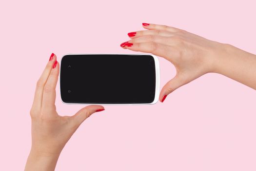 Mobile photography. Female hands with red fingernails holding smartphone isolated on pink background. The evolution of photography.