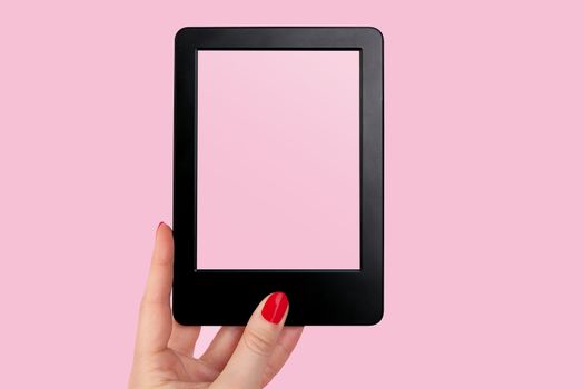 Female hand with red nails holding e reader against pink background. Modern book reading. 