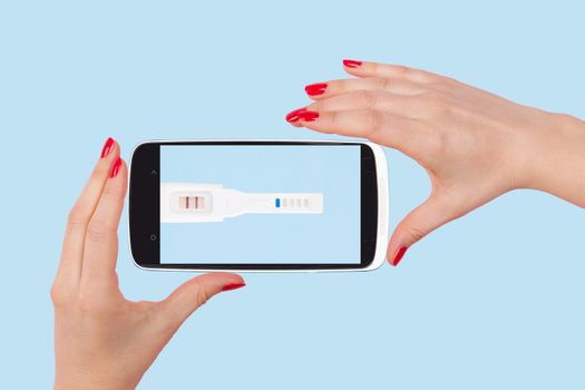 Female hands with red nails holding smartphone with positive pregnancy test isolated on light blue background. The future of medicine.