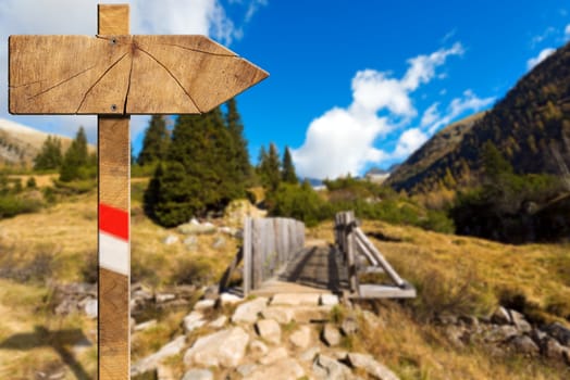 Wooden trail directional sign with one empty arrow in a blurred mountain landscape