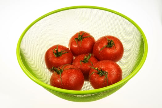 Six red tomatoes in green basket on white isolated background.Tomatoes dewy drops of water.Horizontal view.