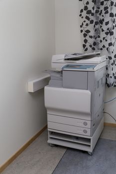 A large printer in an office with curtains in the background