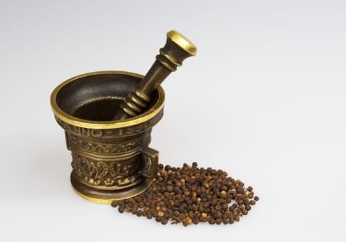 Mortar kitchen with pepper corns on isolated white background.Heavy brass mortar and pestle.Horizontal view.