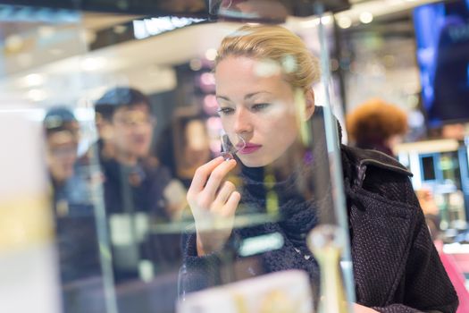 Beautiful blond lady testing and smelling perfume in a beauty store. Woman buying cosmetics in perfumery.