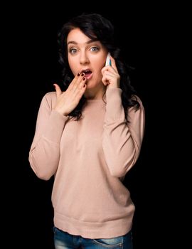 Shocked young woman talking on cell phone on black background