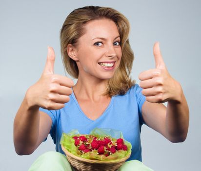 Close up of smiling woman holding raspberries and showing thumb up gesture