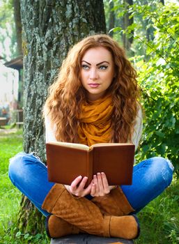 Beaytiful ginger-haired woman reading a book in park sitting on the bench