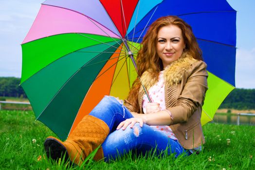 Beautiful smiling red-haired woman with a rainbow umbrella outdoors