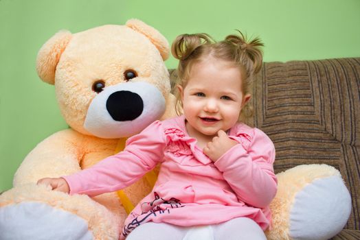 Little girl with big teddy bear sitting on sofa in the living room at home
