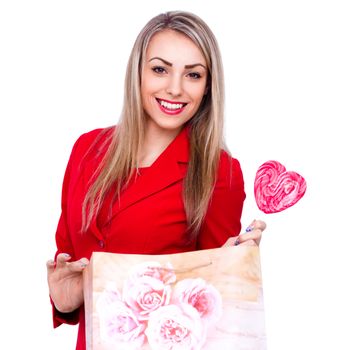 Smiling young woman with heart shaped lollipop and present bag isolated on white