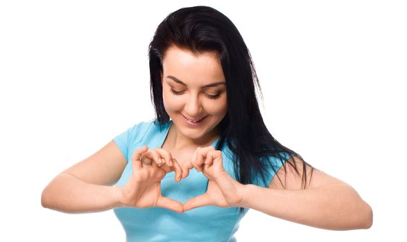 Beautiful young woman showing heart symbol gesture, isolated over white background