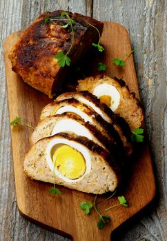 Delicious Homemade Meatloaf Stuffed with Boiled Eggs on Cutting Board closeup on Rustic Wooden background