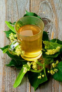 Tea of Linden-Tree Flowers in Glass Cup on Leafs closeup on Rustic Wooden background 