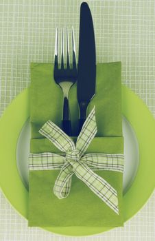 Elegant Table Setting with Fork and Table Knife into Green Napkin Decorated with Checkered Bow on Plate. Retro Styled